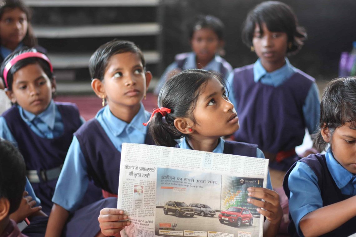 indian students learning in a school with a hindi news paper in hand